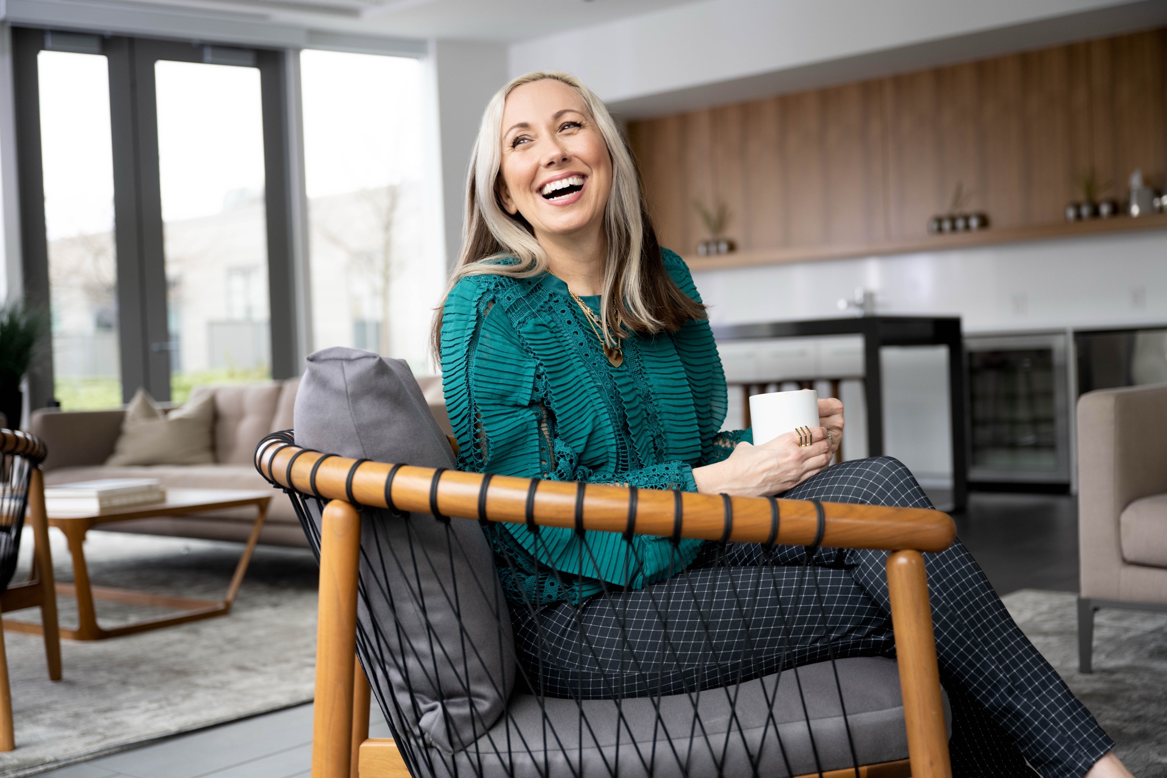 Dill Ward laughing in a mid-century chair with a cup of coffee